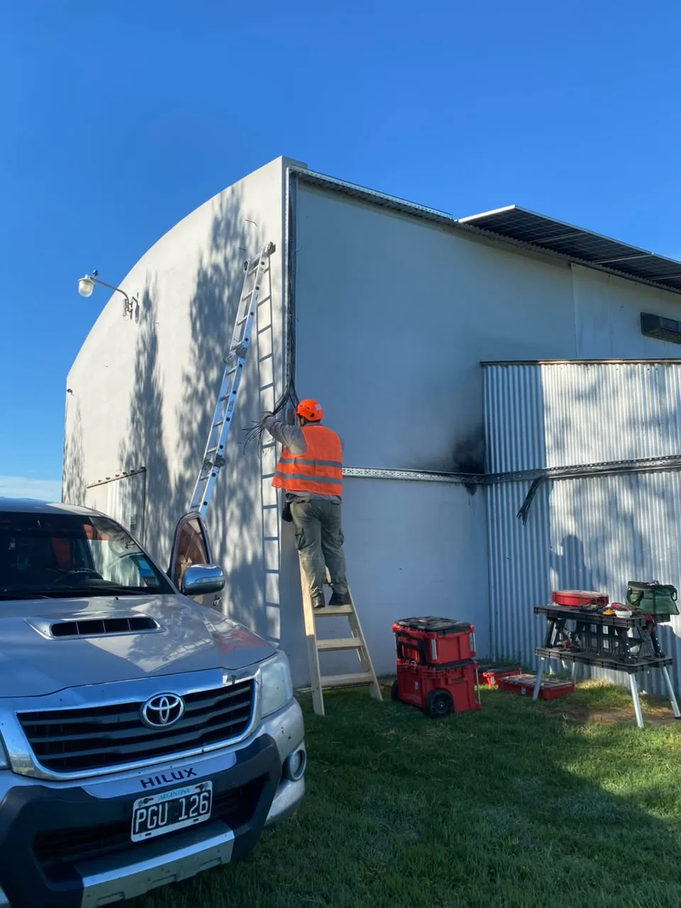 Técnico en escalera cableando la fachada de un galpón