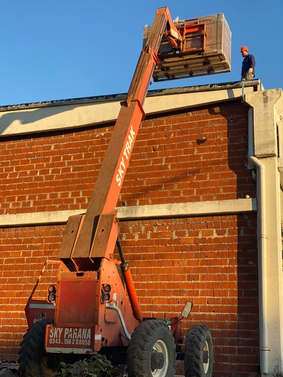 Elevador telescópico subiendo pallets de paneles solares a un techo