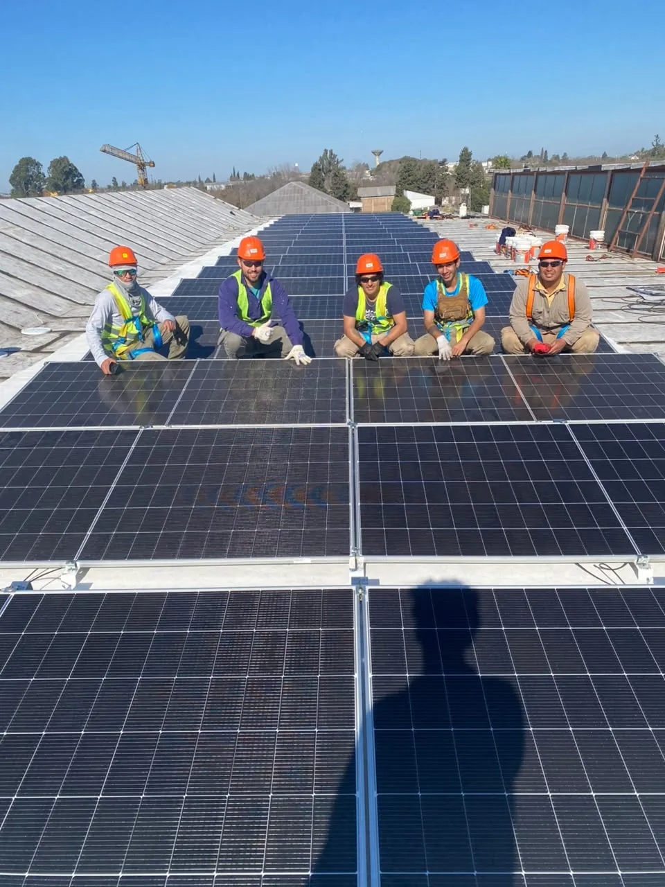 Cinco integrantes del equipo con casco y arnés sobre un techo con paneles solares